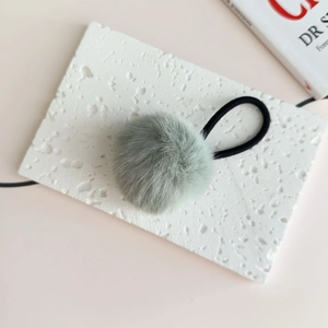 Close-up of a soft mint green pompom hair tie on a decorative stone with high-elastic band