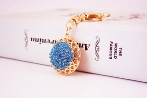 Detailed view of a gold-plated round keychain encrusted with shiny blue rhinestones