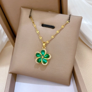 Detail of gold rotating flower necklace with green teardrop stones on display stand