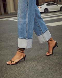 Detail of blue wide-leg jeans with high-waisted folded cuffs and black strappy heels