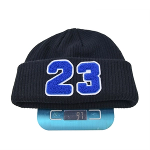 Detalle del gorro de punto negro con parche del número 23 azul y peso mostrado en la báscula