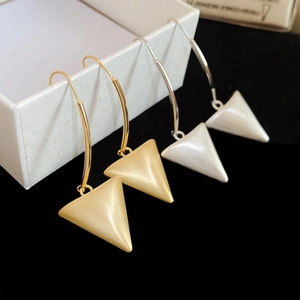 Detail shot of brushed 18k gold and silver triangle earrings on white display box