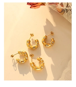 Detailed view of gold C-shaped earrings with pearls and zircon in retro warm lighting