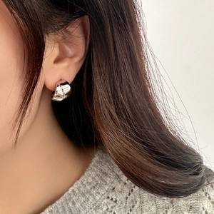 Close-up of model wearing chunky twisted silver hoop earrings with polished mirror finish