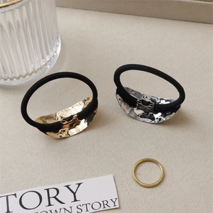 Detail view of gold and silver textured alloy hair ties on a minimalist beige linen surface