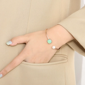 Dettaglio del bracciale C in oro rosa con zircone verde e perla sul polso femminile