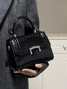 Detail of glossy black crocodile pattern handbag with silver metallic lock clasp and handle