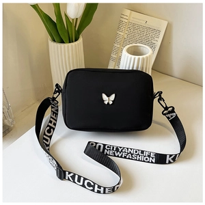 Detail of black nylon shoulder bag with butterfly charm and lettered wide strap