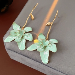 Detail of vintage gold branch earrings with light green enamel flower petals on grey fabric