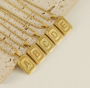 Détail de cinq pendentifs lettres carrés en acier inoxydable 18K sur chaînes torsadées