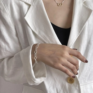 Close-up of a minimalist 925 sterling silver chain bracelet worn by a model in a white suit