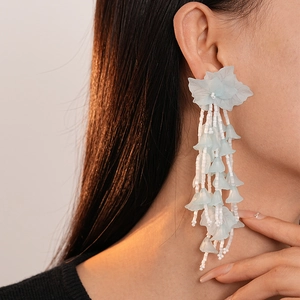 Close-up of light blue frosted flower earrings with beaded tassels on a model