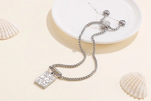 Detail of adjustable silver square chain bracelet with symbolic pendant and heart charm