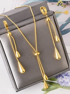 Close-up of golden teardrop pendant jewelry set on dark grey leather display