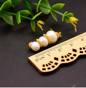 Macro shot showing a 2cm triple pearl earring with gold wire wrap next to a ruler