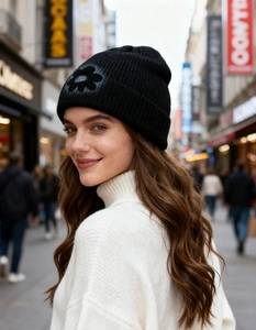 Outdoor street style shot of a black knit beanie featuring a hand-painted flower pattern