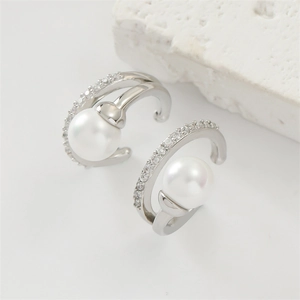 Detail of silver ear clips with pearl and diamond inlays on a white stone background