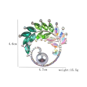 Detailed view of silver crystal brooch with marquise green gems and a grey pearl dangle