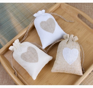 Three small linen drawstring jewelry pouches with stitched heart motifs on a bamboo tray