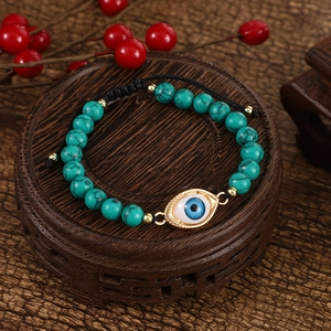 Handmade turquoise beaded evil eye bracelet with adjustable black braided cord on wood