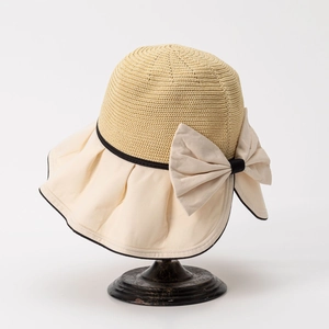 Detail of a beige straw hat with a large bow on a vintage stand, showing fabric textures