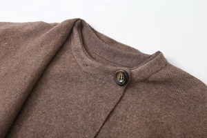 Dettaglio ravvicinato dello scollo del maglione in maglia marrone con bottone marmorizzato