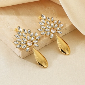 Detailed shot of golden leaf earrings with clear crystals on a beige stone background