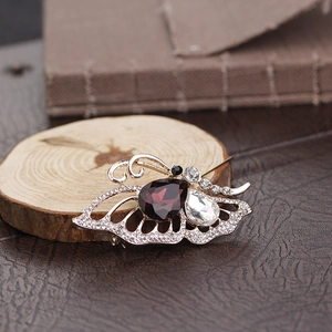 Macro detail of golden butterfly brooch with ruby red and clear crystals on wood