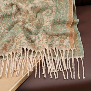 Detail shot of beige core-spun yarn scarf with orange paisley patterns and long tassels