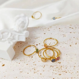 Detail of slim gold birthstone rings with multi-color gems on a textured beige tray