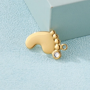 Gold baby footprint pendant in stainless steel with a clear zircon on a blue surface