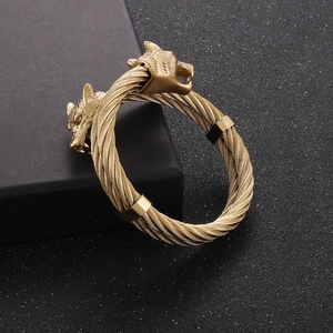 Detailed close-up of golden dual wolf heads and braided cable wire band on punk style bracelet
