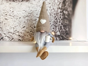 Close-up of a Christmas gnome with brown knitted heart hat holding a white coffee mug