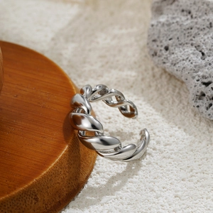 Macro detail of silver twisted open ring on textured stone and wooden coaster