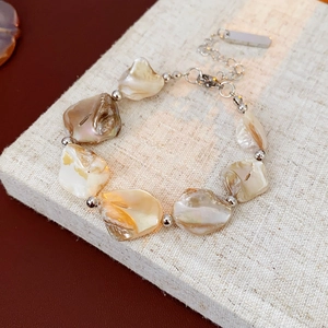 Gros plan d'un bracelet en perles beiges irrégulières et chaîne argentée sur tissu