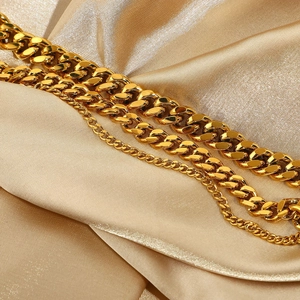 Detail of gold Cuban and curb link anklets on champagne silk fabric background