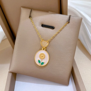 Macro detail of gold necklace with rhinestone heart and sunflower oval pendant