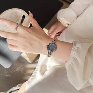 Close-up of elegant silver chain watch with blue dial and diamond ring on a silk dress background