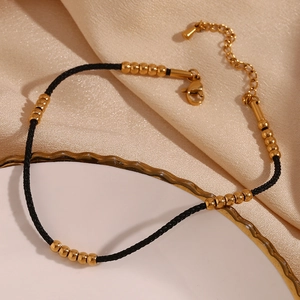 Detail of 18K gold plated beads on black cord anklet with lobster clasp on silk