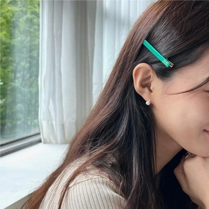 Close-up of a vibrant green barrette with white text worn on deep brown wavy hair