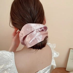 Close-up of pink satin scrunchie showing glossy fabric texture and soft pleated folds