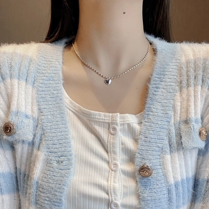 Close-up of minimalist silver heart necklace with beaded chain on female model neck