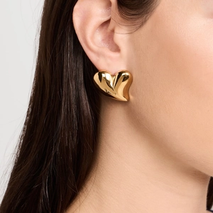 Close-up of heart-shaped gold earring worn on ear with polished stainless steel finish
