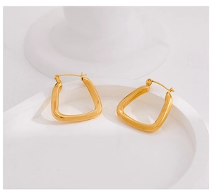 Macro detail of glossy gold-plated geometric U-shaped earrings on a white display tray