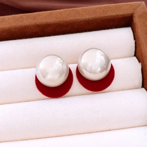 Macro shot of large round white pearl earrings with red velvet base on canvas backing