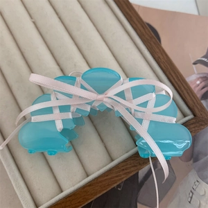 Close-up of a light blue acetate hair claw clip with a pink ribbon bow on a jewelry tray