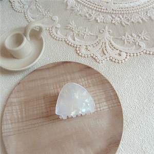 Close-up of triangular pearl white acetate hair claw on elegant lace and wood background
