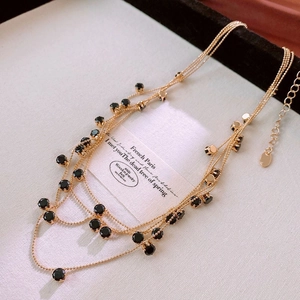 Macro view of multi-layered golden beaded necklace with black round stones and logo tag