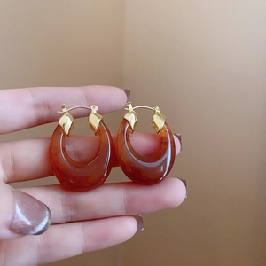 Close-up of amber resin earrings with gold metal needles held in hand for detail