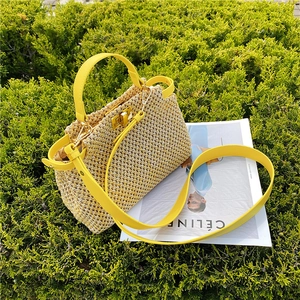 Detail of yellow straw bag with metal twist lock and leather handles against green shrubs
